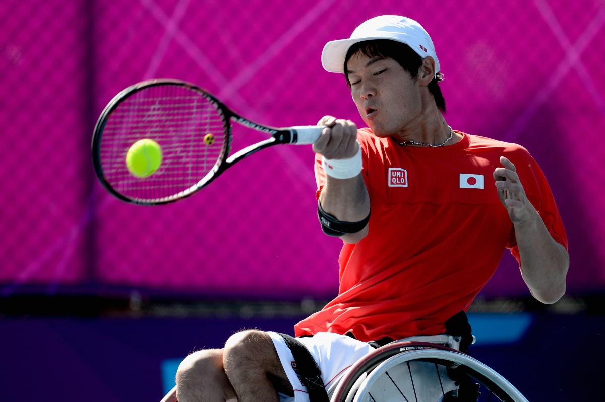 A picture of man in a wheelchair playing a forehand in a tennis match