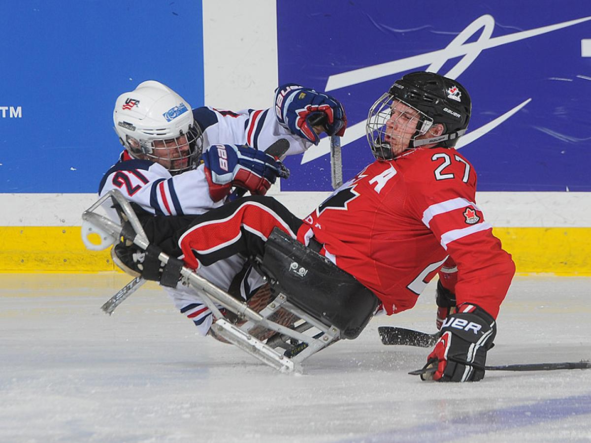 A picture of two men in sledges playing ice hockey