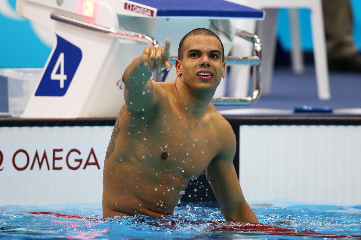 A picture of a man in the pool sitting on the swimming line with his hand up 