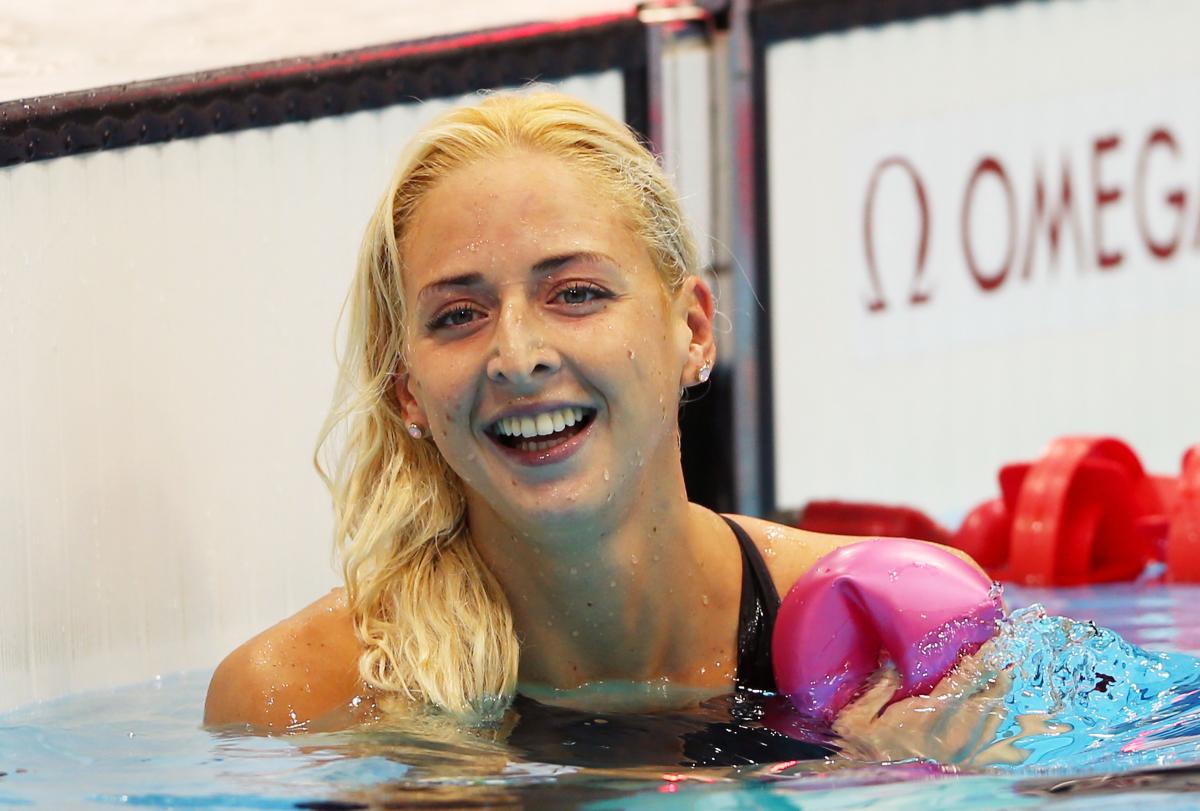 A picture of a woman in the pool holding the swimming cap with her hand