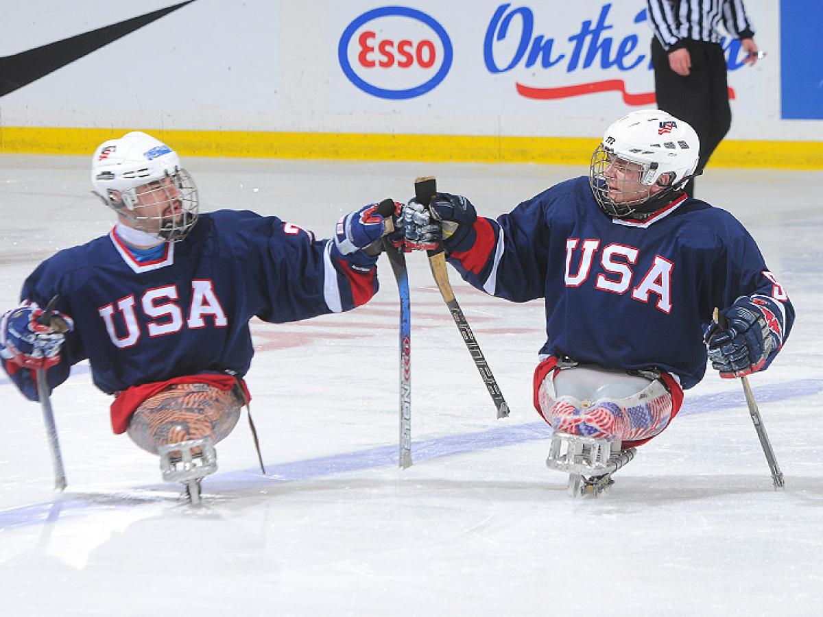 A picture of 2 mens in sledges during an ice sledge hockey match