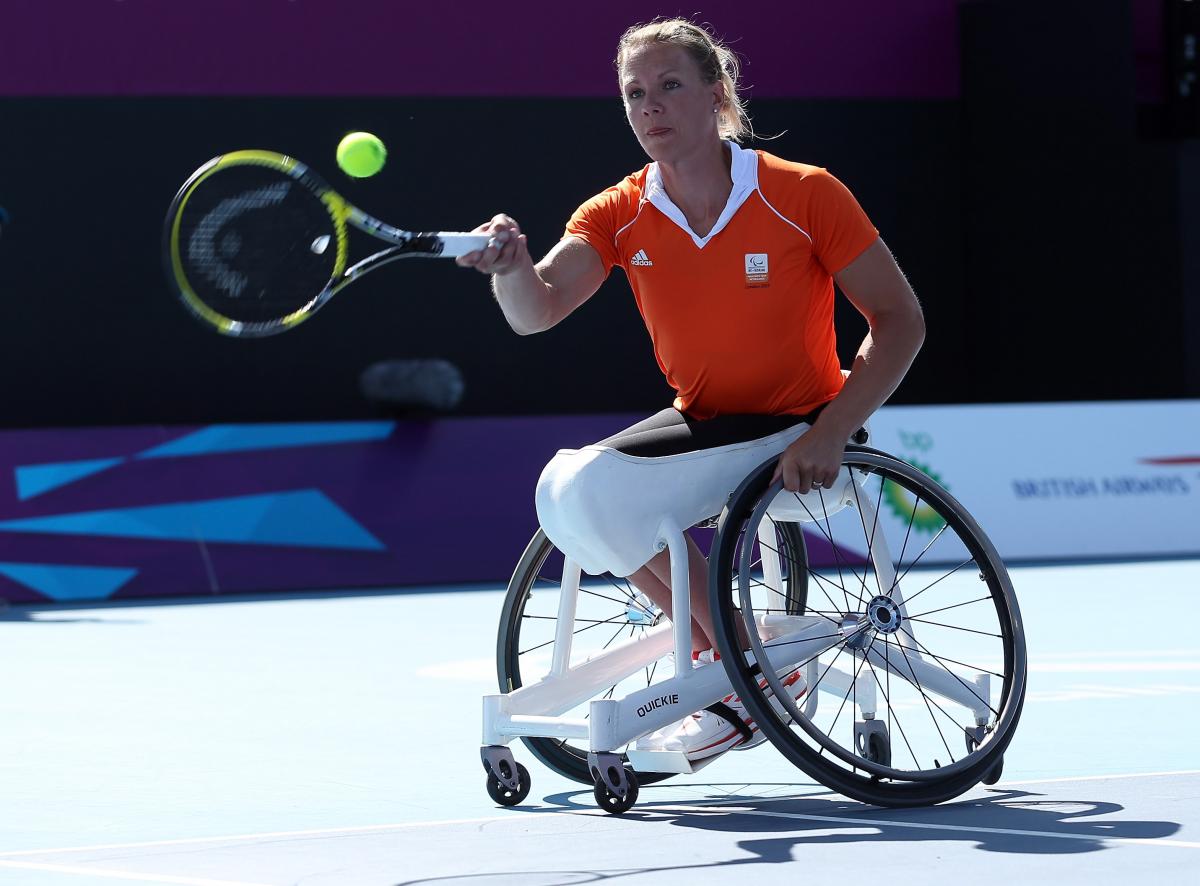 A picture of a woman in a wheelchair playing a forhand during a wheelchair tennis match.