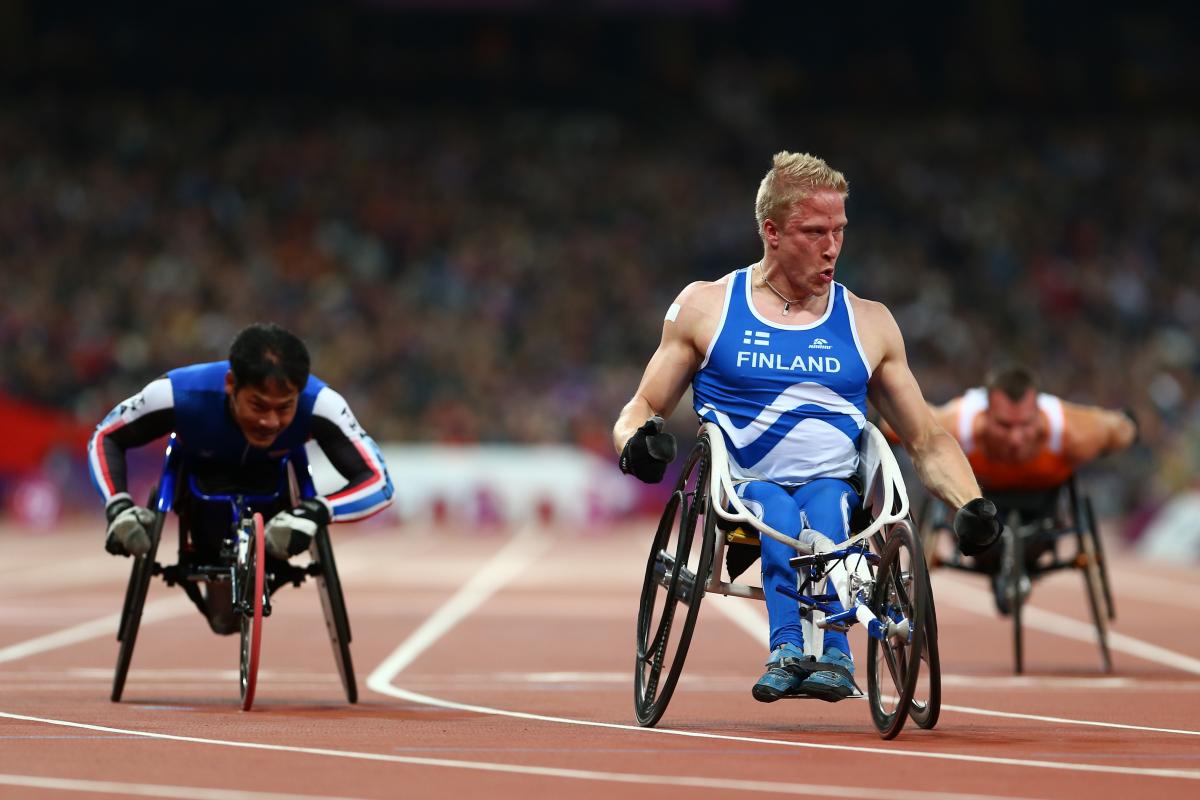 A picture of a man in a wheelchair celebrates on a track after crossing a finish line
