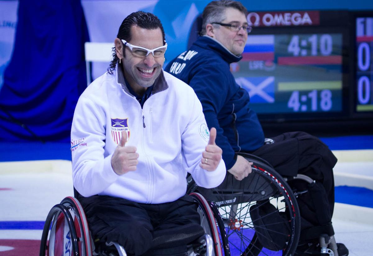 A picture of a man in a wheelchair tumbs up celebrating his victory