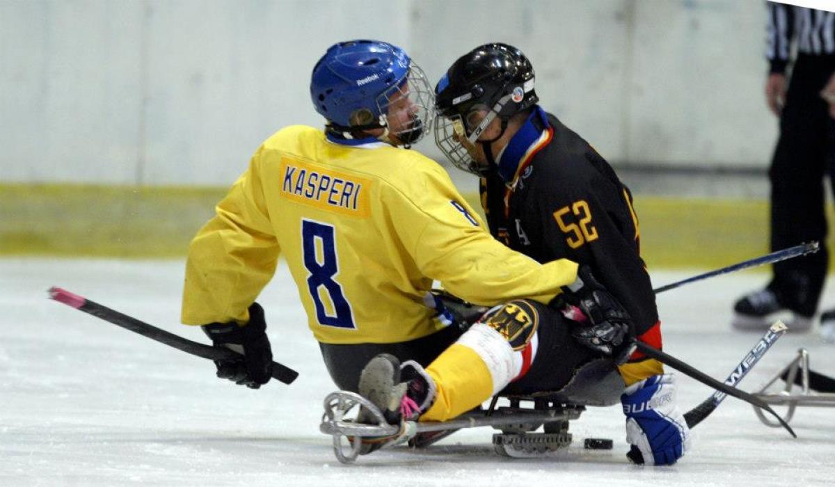 A picture of 2 men in sledges playing ice hockey
