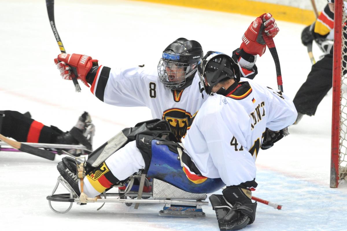 A picture of 2 men in sledges celebrating a goal during a ice sledge hockey match