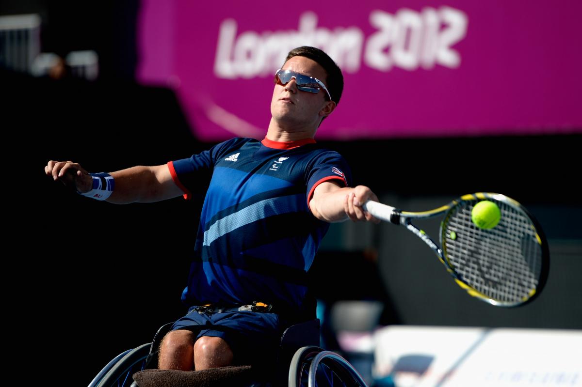 A picture of a man in a wheelchair playing a forehand during a wheelchair tennis game