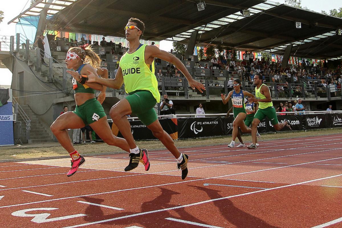 Terezinha Guilhermina and her guide run on the track of Lyon with the tribunes of the stadium in the backround