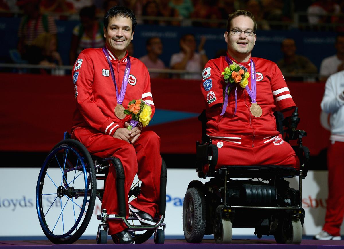Two boccia player sit in the wheelchairs with their medals around their neck.
