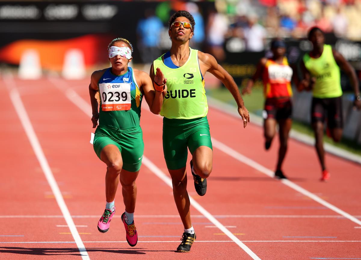 A visually impaired athlete runs with her guide on the track of a stadium.