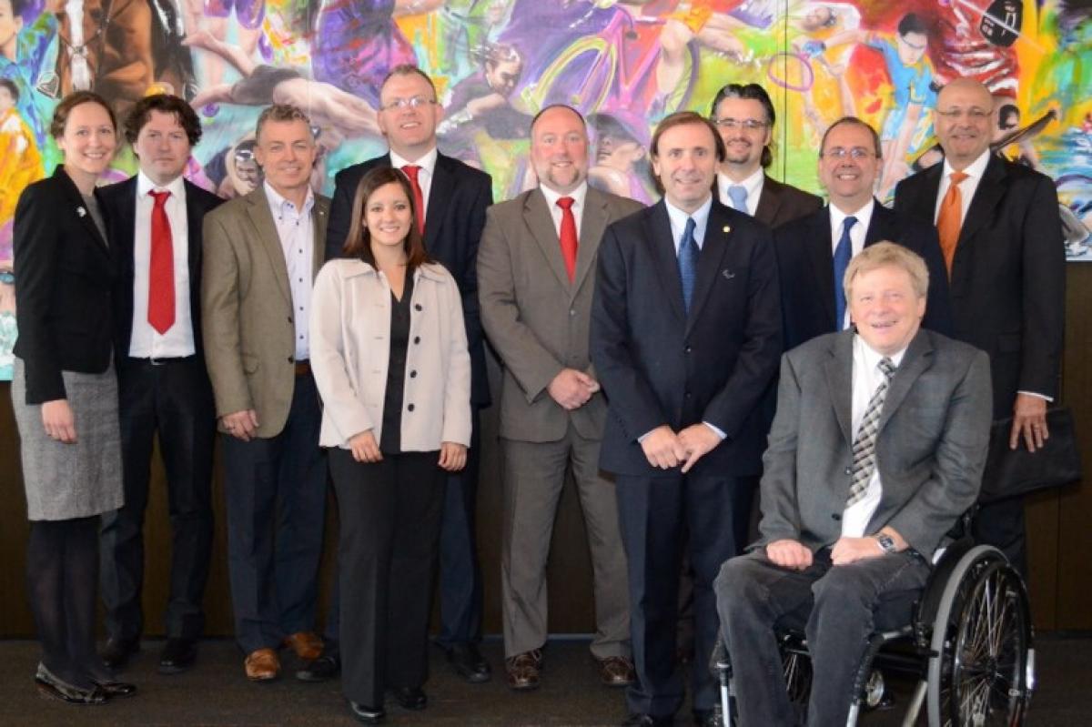 Toronto 2015 Co-ordination Commission May 2014 A group shot of 11 smartly dressed people lined up in front of a painted sport wall mosaic looking directly at the camera