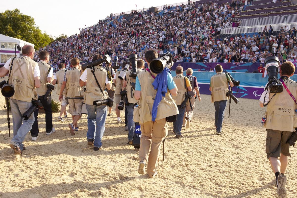 A group of photographers' backs are shown as the walk across an equestrian venue.