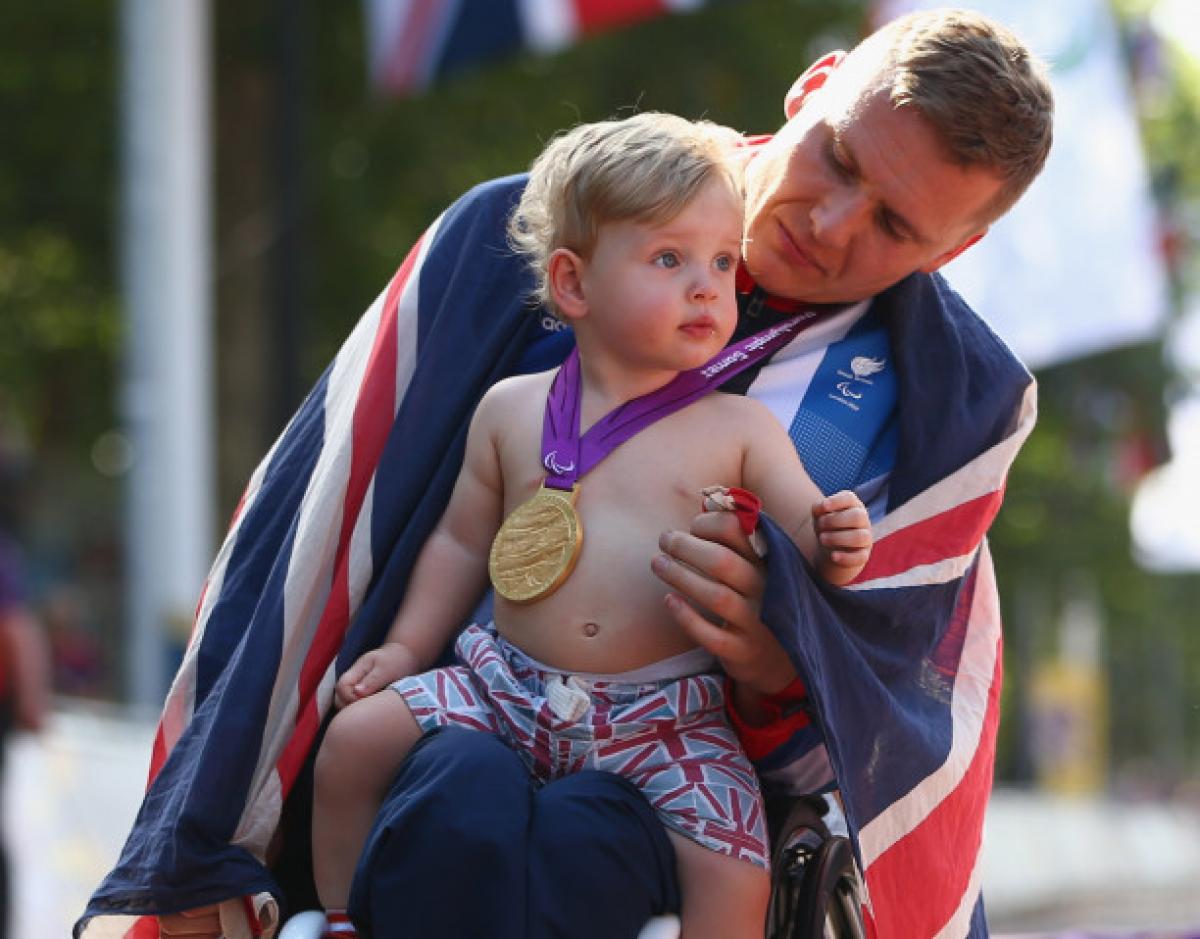 A picture of man in a wheelchair holding his baby after his victory