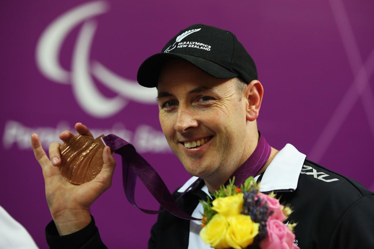 Michael Johnson New Zealand London Portrait of smiling man wearing a basecap showing his bronze medal to the camera.