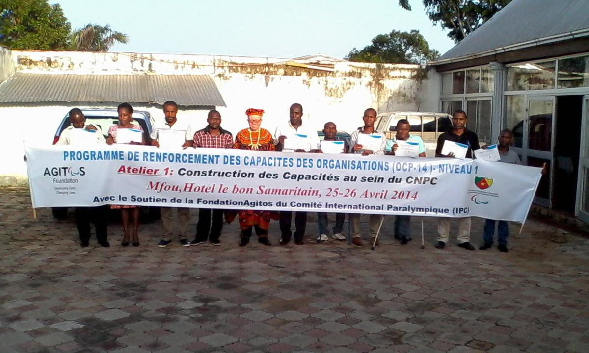 A group shot of people standing and sitting in wheelchairs behind a banner with the following text: Programme de renforcement des capacites des organisations - Niveau 1