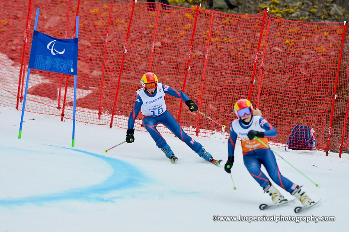 Two skiers in race suits going down a slope