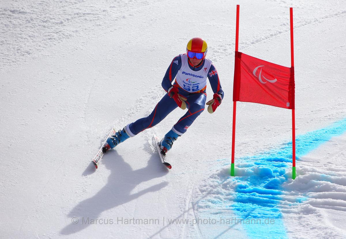 Skier in navy and white ski suit and red helmet skis past a giant slalom gate