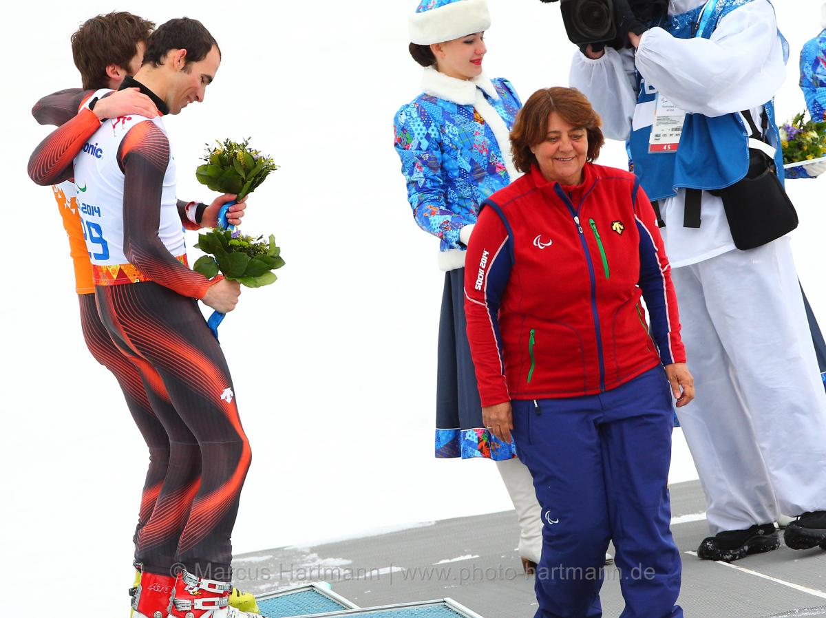Two skiers on a podium with a women presenting them their medals