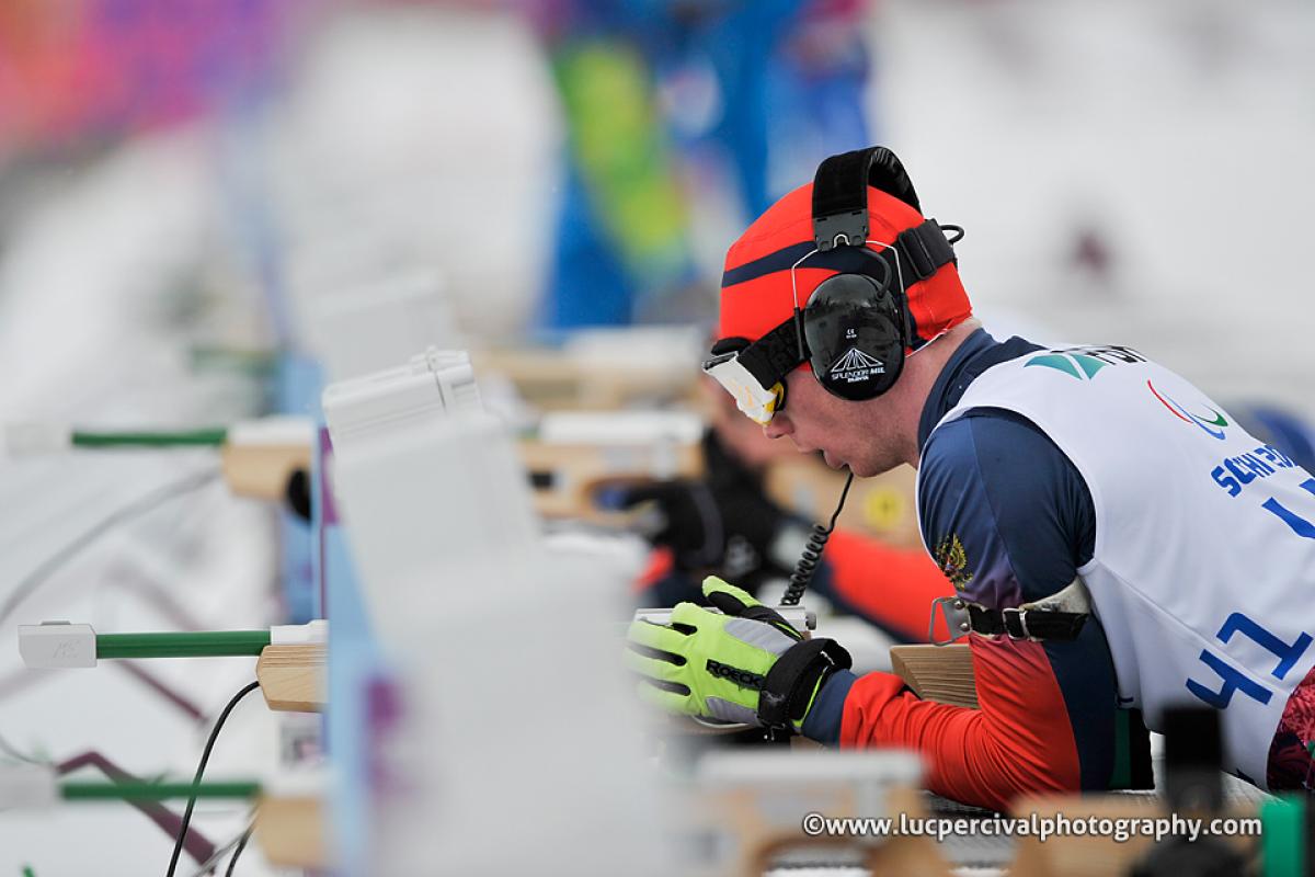 Athlete with ear phones takes aim in biathlon.