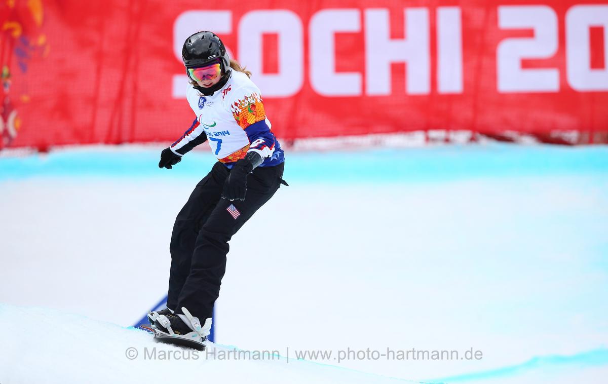 Snowboarder Nicole Roundy rides down course with Sochi 2014 banner in background