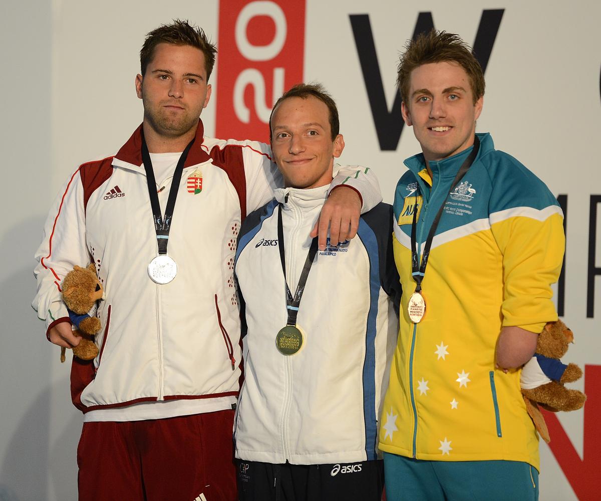 Three swimmers in their team dresses on the podium wearing medals, putting their arms around each other