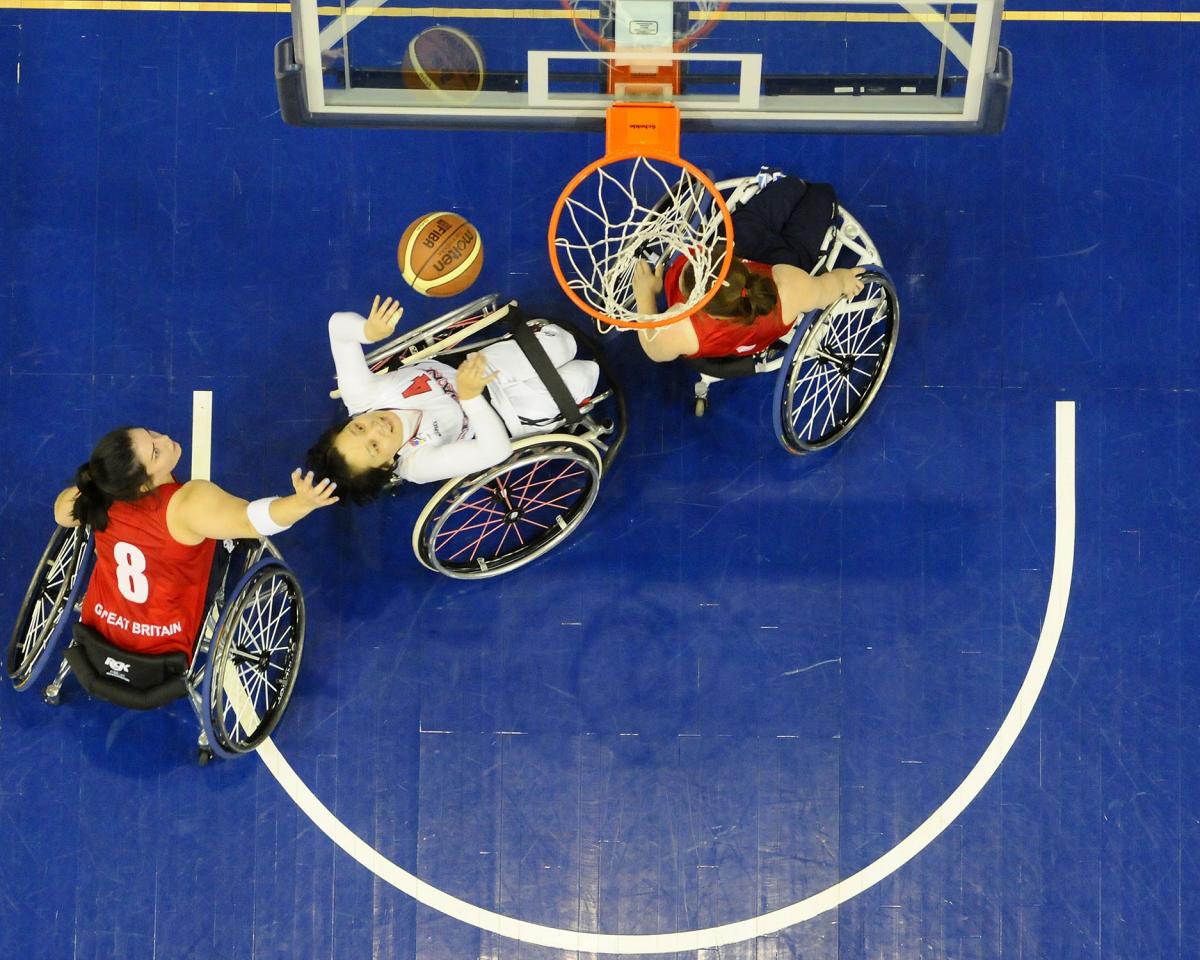 Great Britain v Japan 2014 Women’s World Wheelchair Basketball Championships Picture taken from above the basketball basket. Three female players in wheelchairs fighting for the ball under the basket.