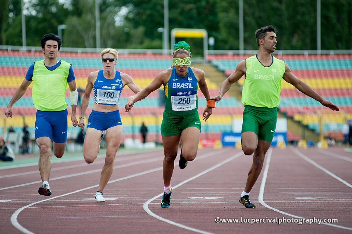 Two blindfolded women running on a track with their male guides. All wearing running suits