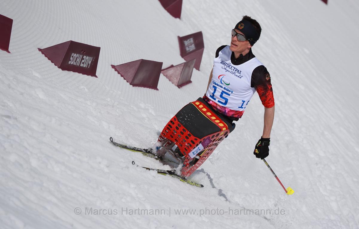 A sit skier rounds a bend in the course in the stadium in Sochi, pushing forward at speed.