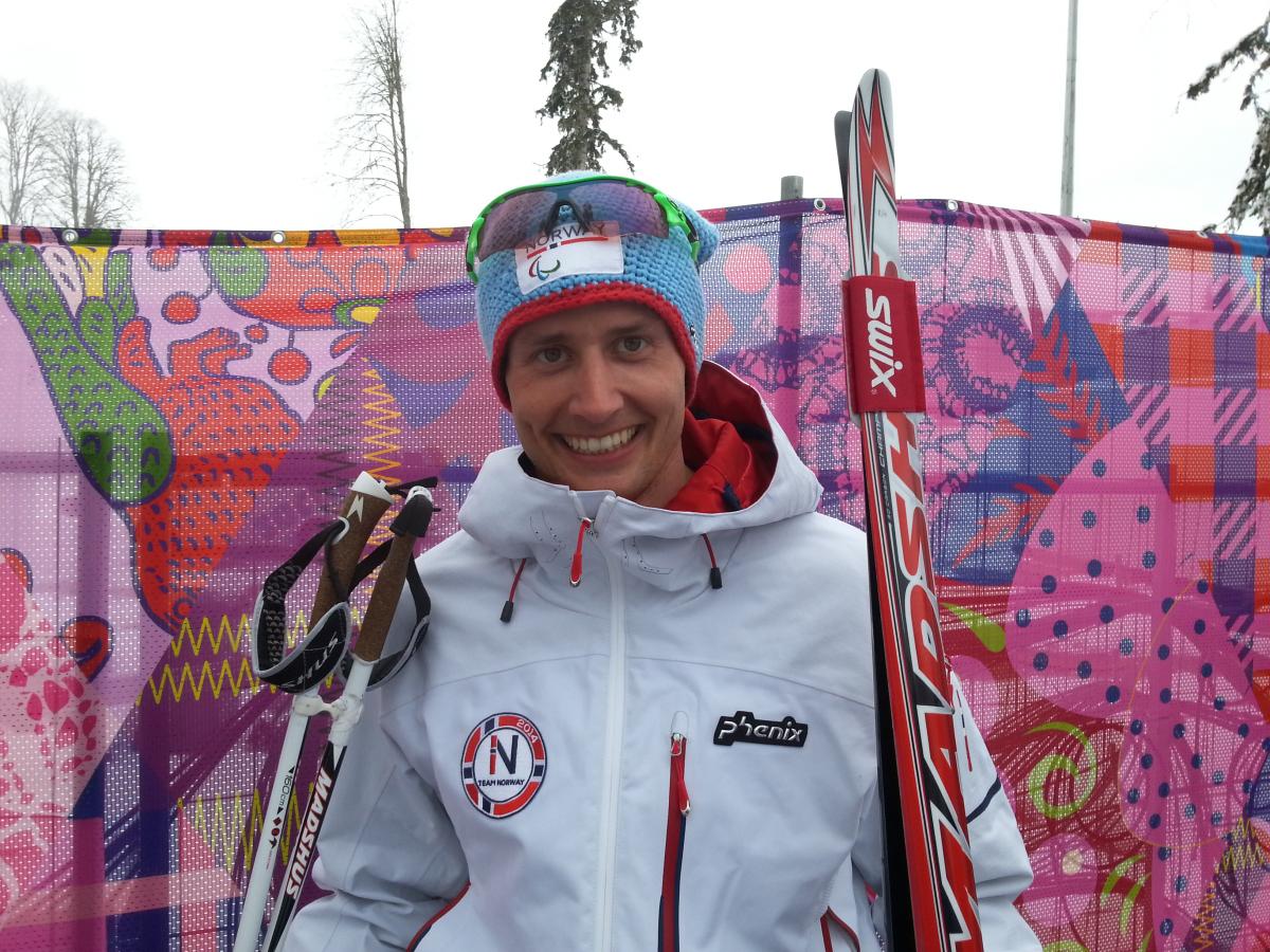 Young man holding cross-country skies smiling to the camera