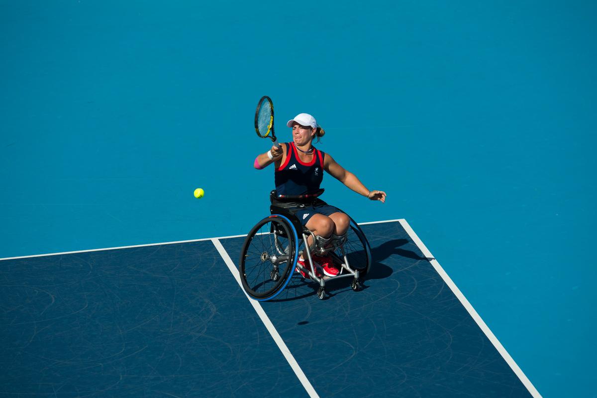 Woman in wheelchair playing tennis on a blue court