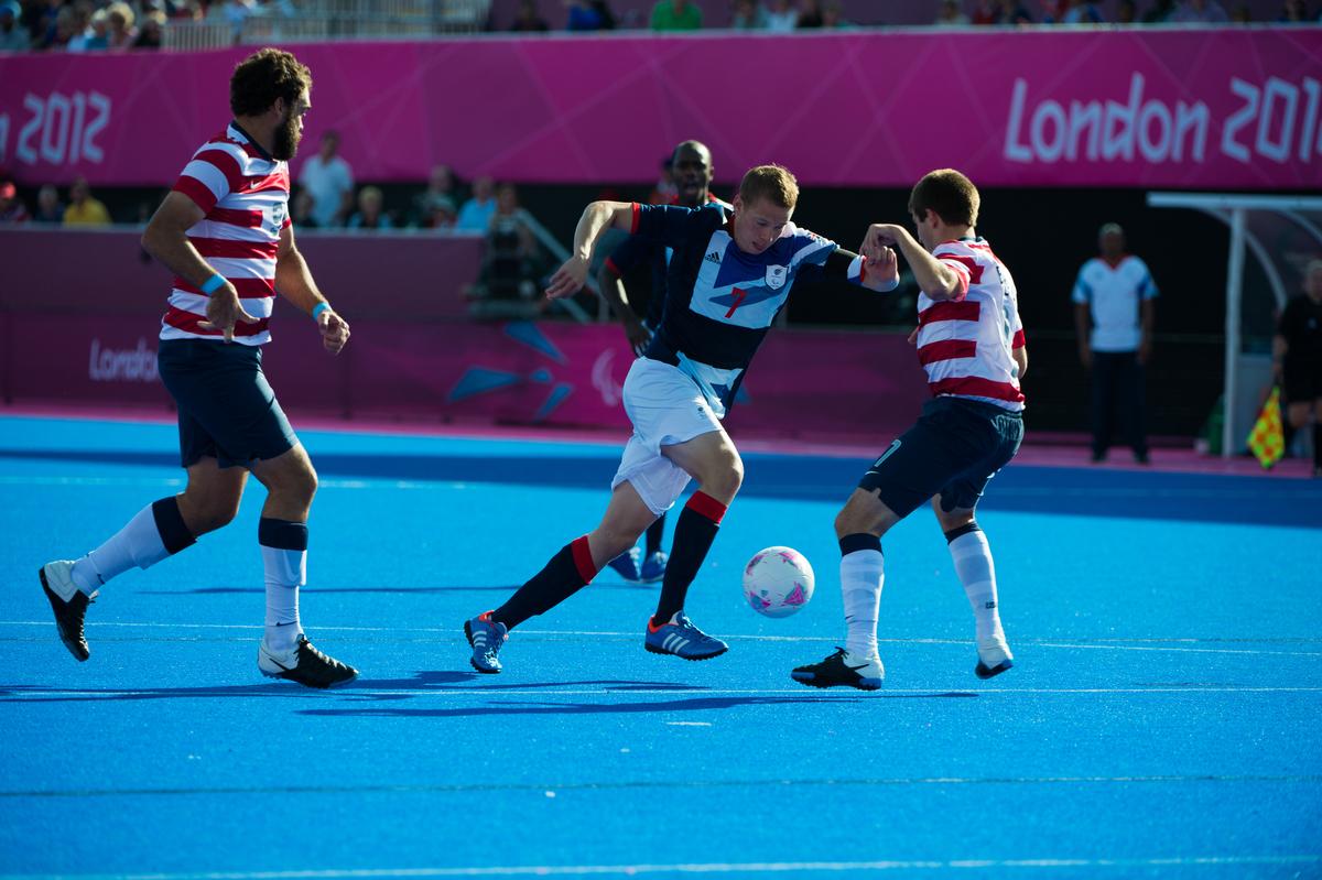 Michael BARKER - Football Seven-a-Side - London 2012 Paralympic Games Defender trying to stop a football player on a blues field of play