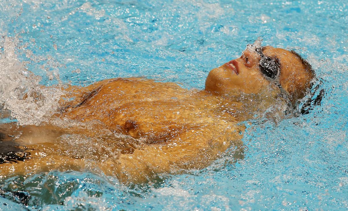 Dmitrii Kokarev A swimmer wearing goggles laid on his back in the water at the start of a race.