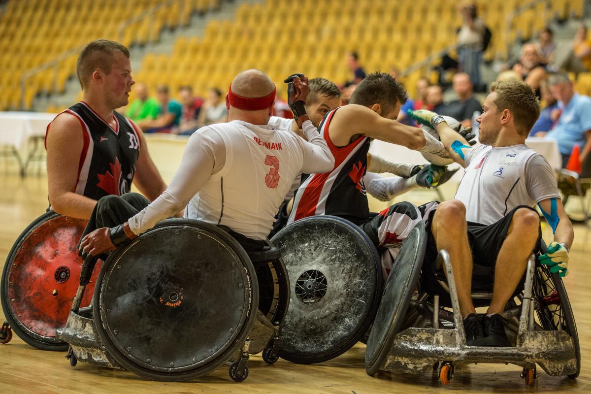 A group of four players in wheelchairs - two per side - fight for the ball during a wheelchair rugby match.