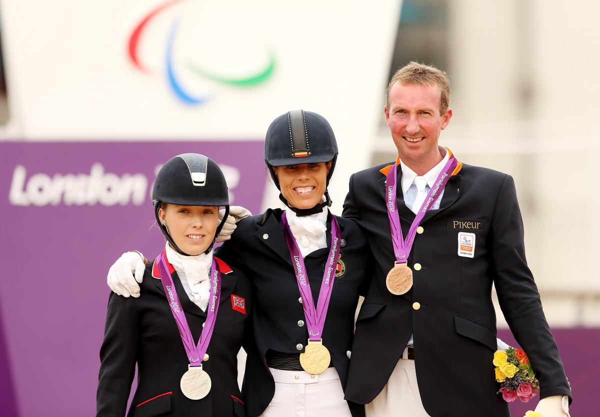 Two women and one man in dressage uniforms standing on the medals podium.