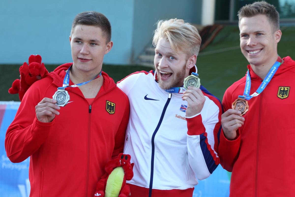 3 upper bodies of athletes on the podium, posing and showing their medals.