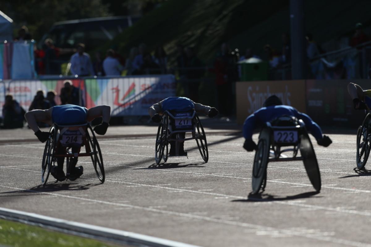 Wheelchair athletes race on a track, photographed from the back