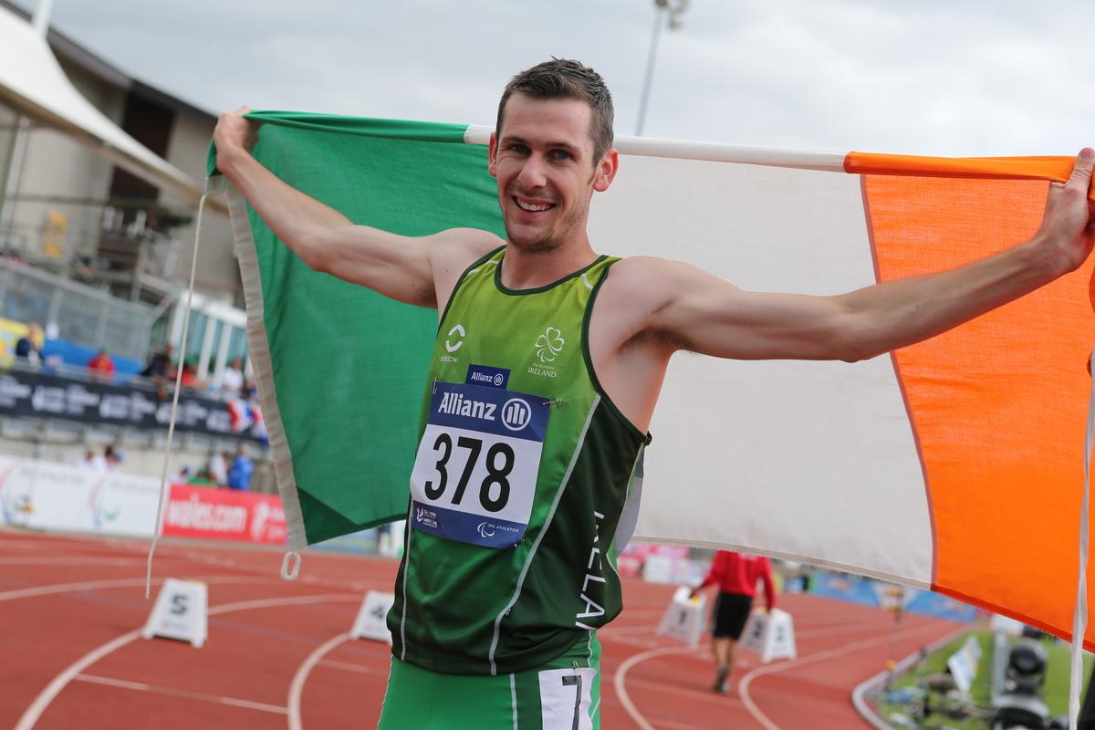 Man in green shirt holding an Irish flag and smiling to the camera