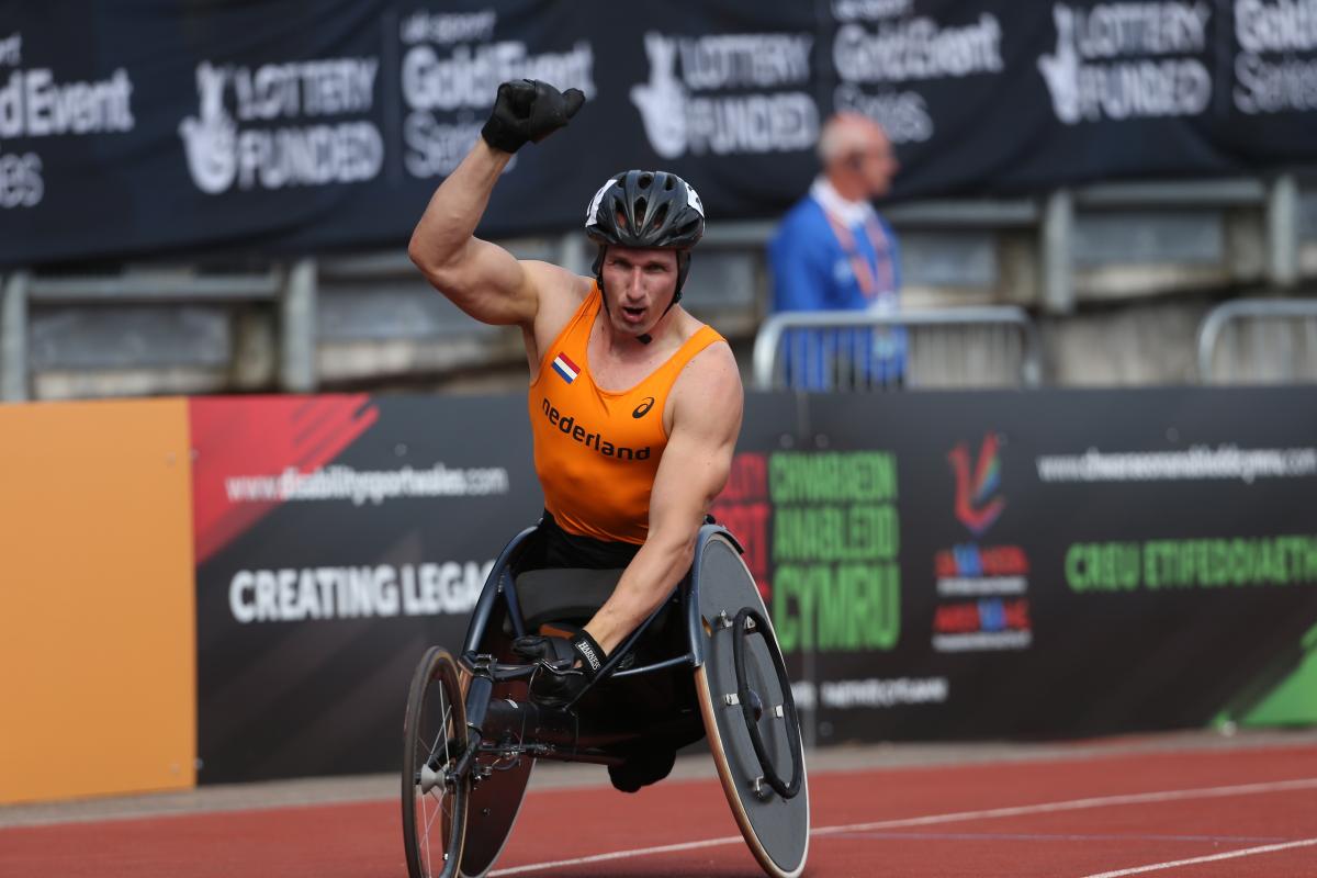 Man in racing wheelchair holding a Dutch flag, celebrating