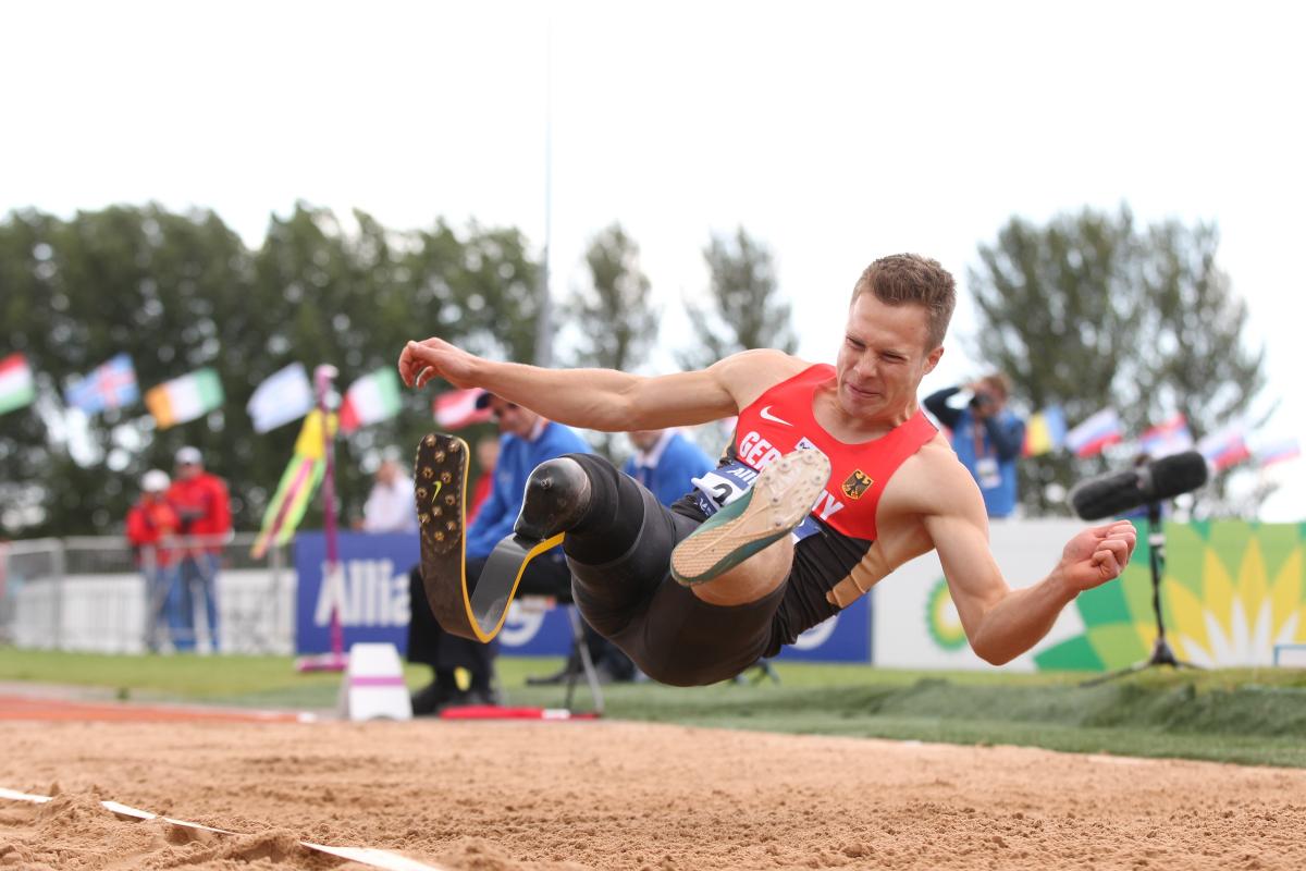 Man in the long jump right before landing in the sand