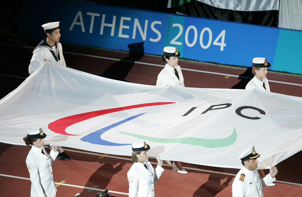 Six people carry a flag with the Paralympic symbol into a stadium