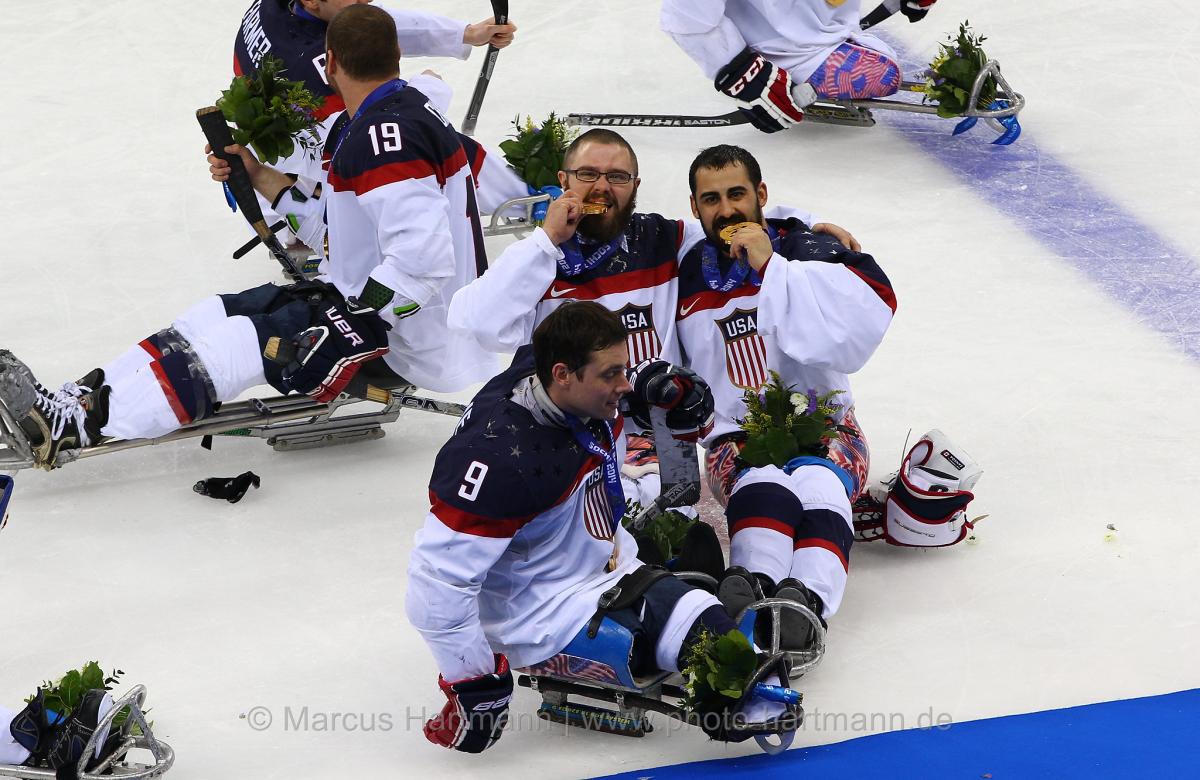 Four sledge hockey player on the ice, posing for a camera with their gold medals