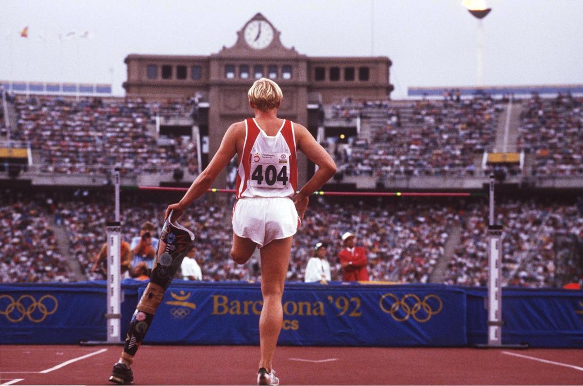 High jumper looking at the bar while holding a prosthetic leg in his hand.