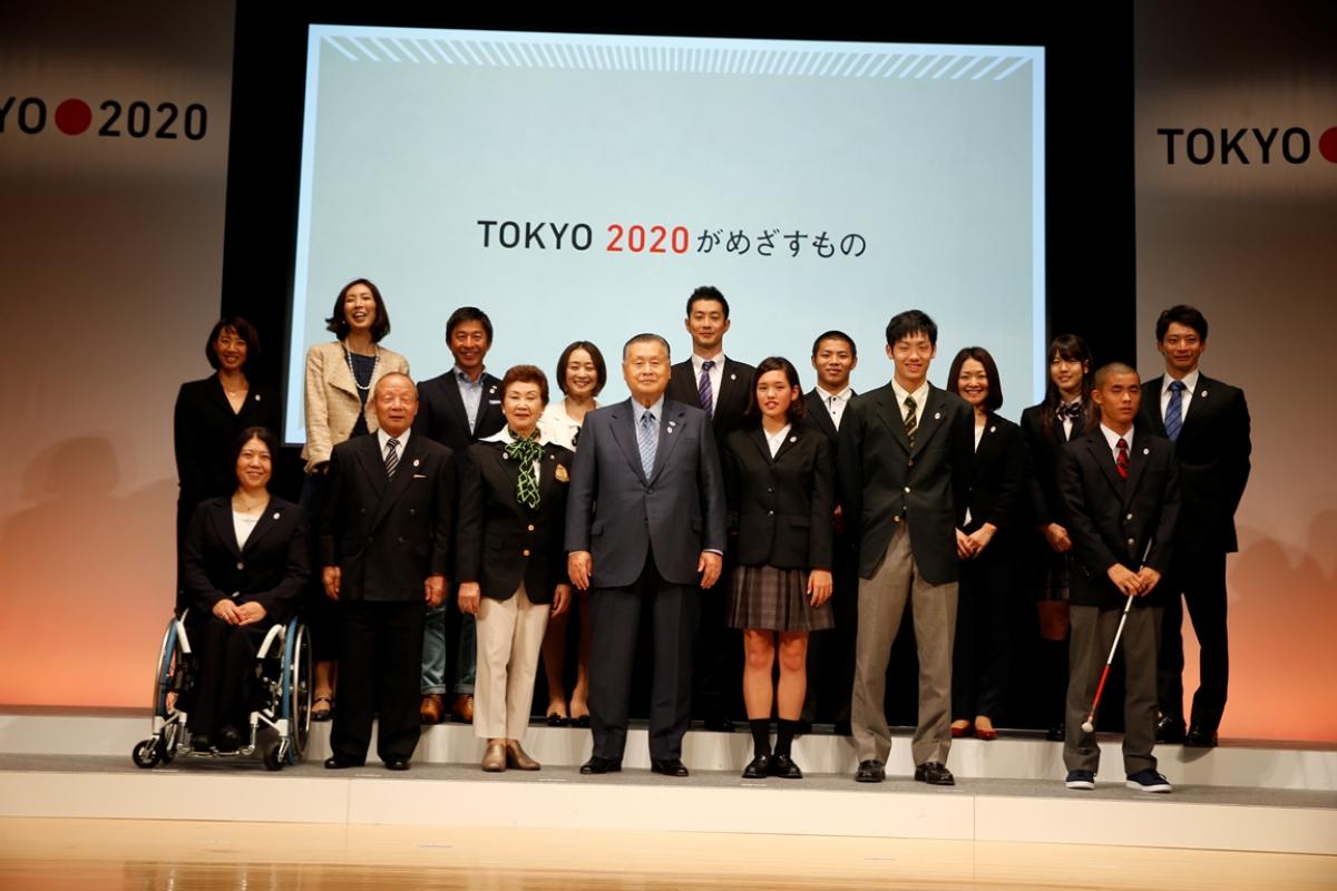 Japanese people standing in a line under a Tokyo 2020 banner