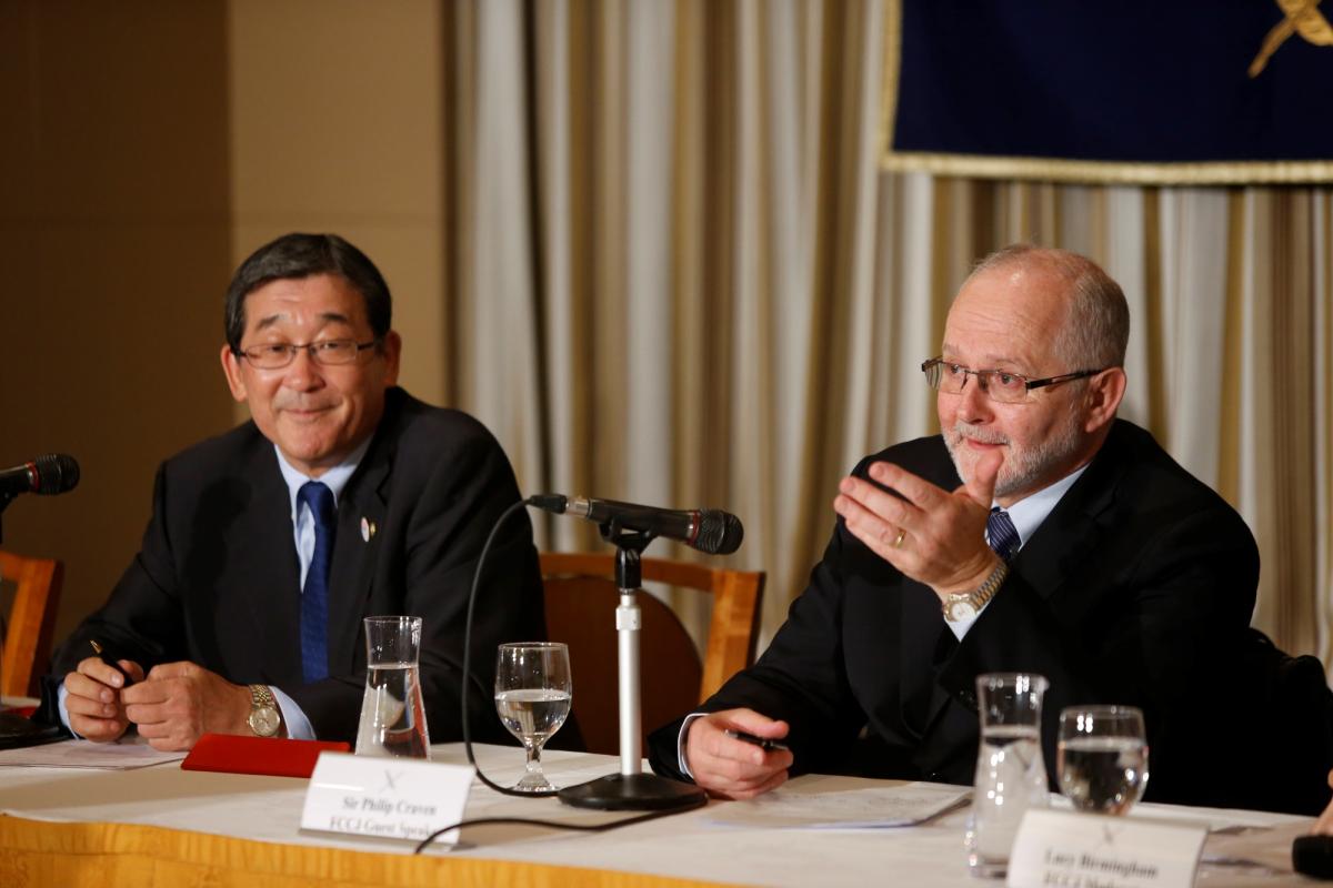 Two men sitting on a podium behind a table with microphones in front of them