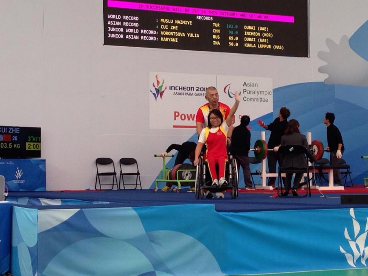 Women in wheelchair waving in front of a bench press