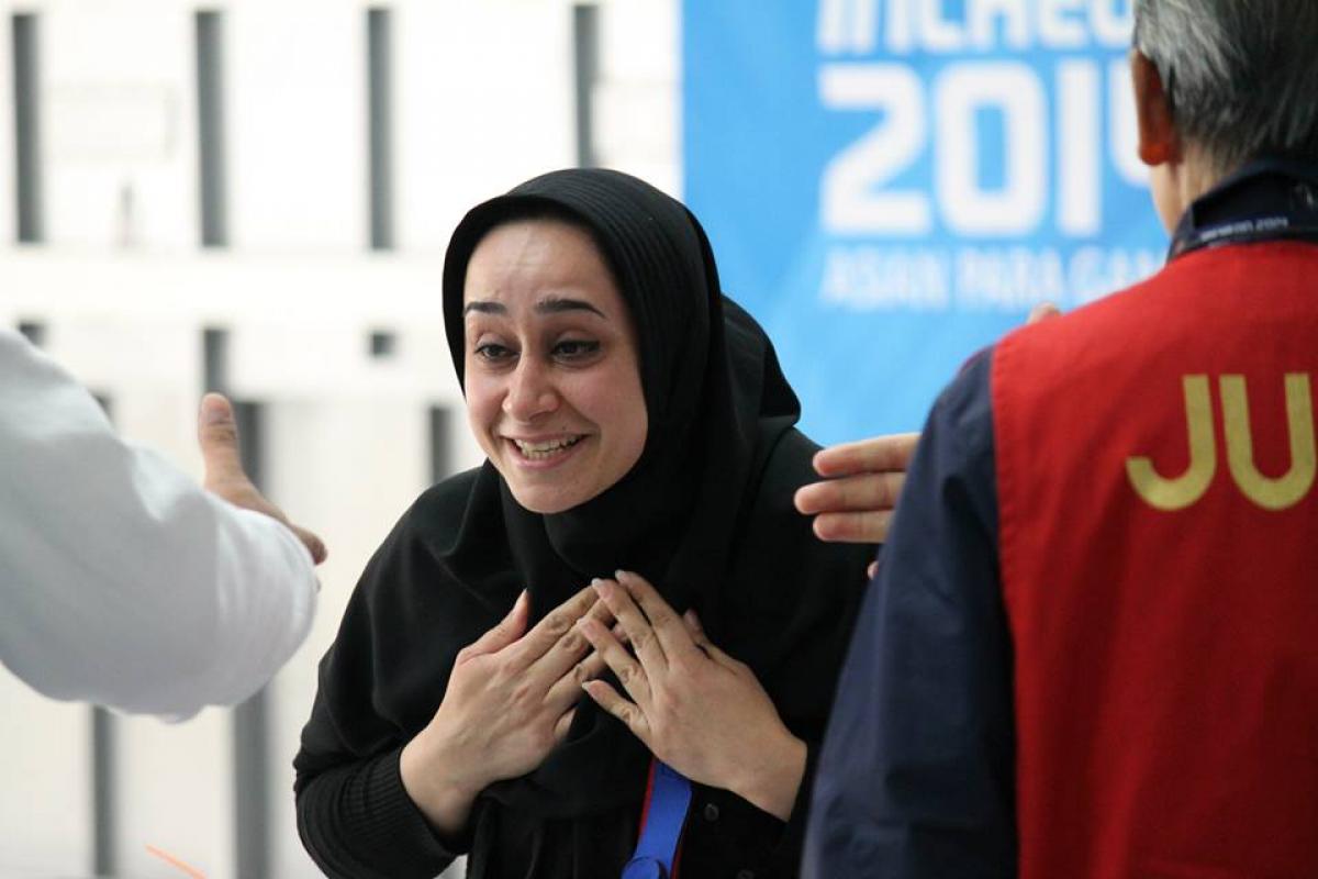 Women wearing a headscarf looks surprised and happy in front of a Incheon 2014 Asian Para Games banner