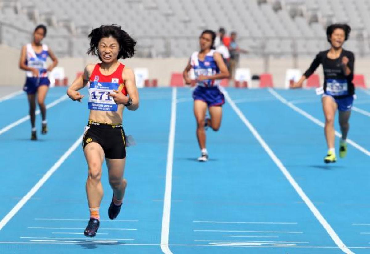 Female runner crosses the finish line on a blue track in a stadium, celebrating