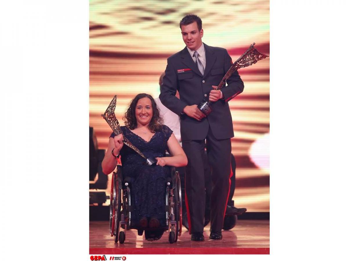 Women in wheelchair, man walking both holding a trophy in their hands