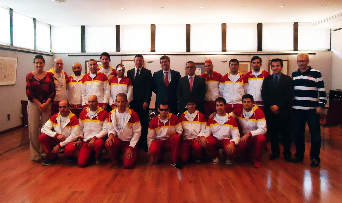 Group shot of a football team in training suits with six people in business clothes.