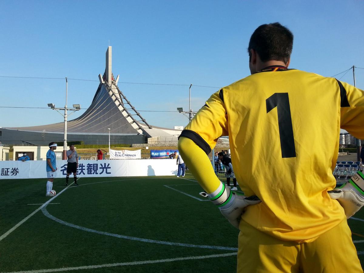 Back of a football player looking at another blindfolded player who prepares to shoot a penalty